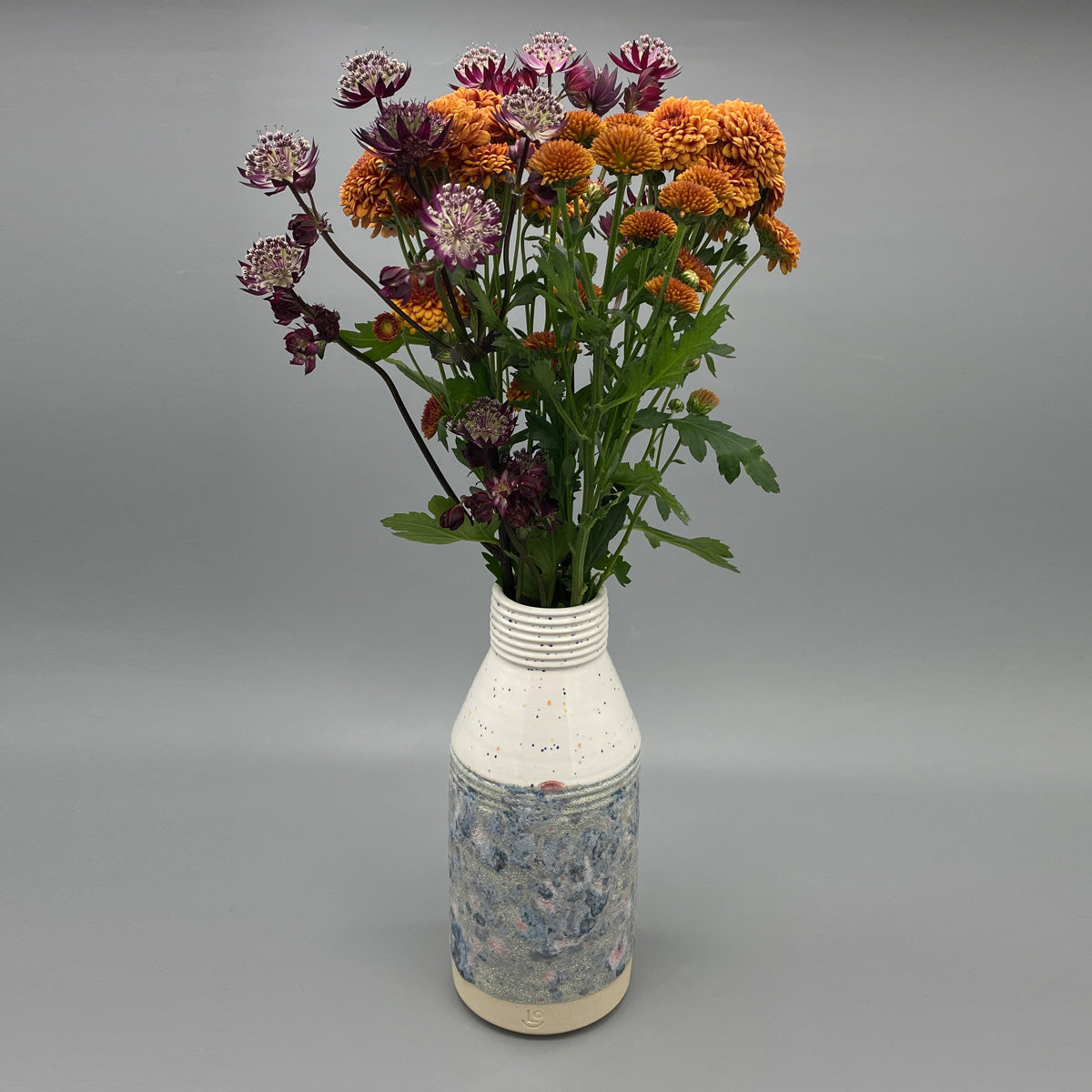 A ceramic vase with a wide neck and textured body featuring a speckled upper half and a mottled blue and grey lower half.