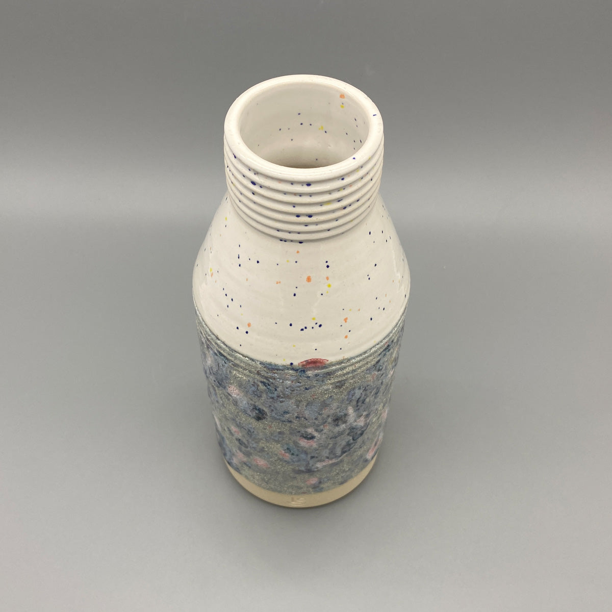 A ceramic vase with a wide neck and textured body featuring a speckled upper half and a mottled blue and grey lower half.