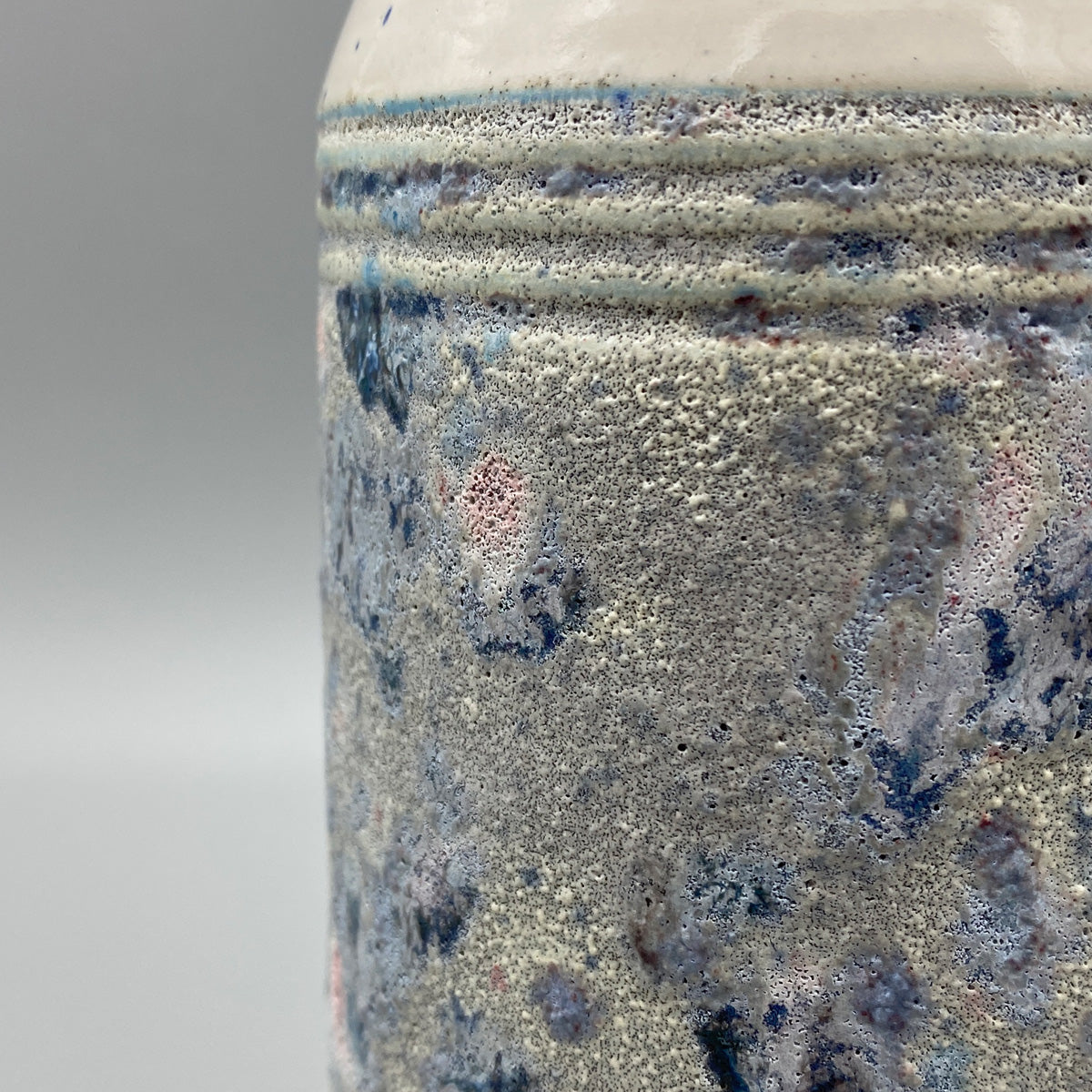 A ceramic vase with a wide neck and textured body featuring a speckled upper half and a mottled blue and grey lower half.
